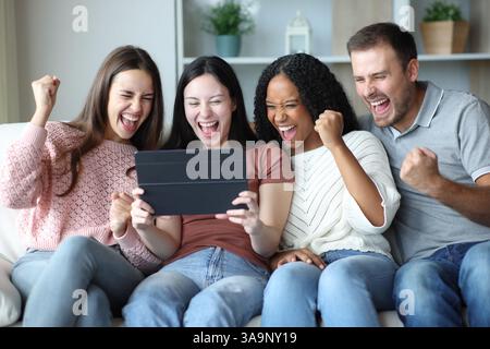 Excited group of friends celebrating good news checking tablet content at home Stock Photo