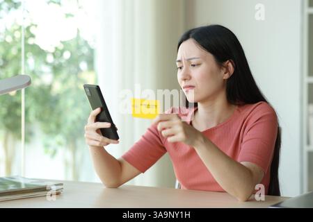 Sad asian woman buying online using phone and credit card sitting in a room Stock Photo
