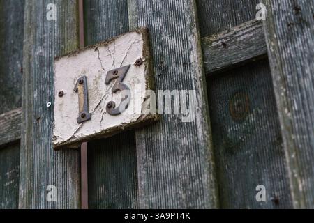 Rusty number 13 and white plate on a rough raw green wooden fence mounted with screws Stock Photo
