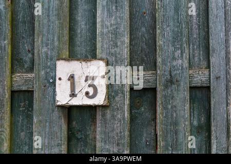 Rusty number 13 and white plate on a rough raw green wooden fence mounted with screws Stock Photo