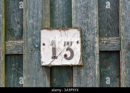 Rusty number 13 and white plate on a rough raw green wooden fence mounted with screws Stock Photo