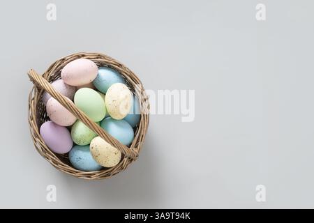 Easter pastel eggs in wicker basket for Happy holiday on gray background. View from above. Greeting card with copy space. Stock Photo