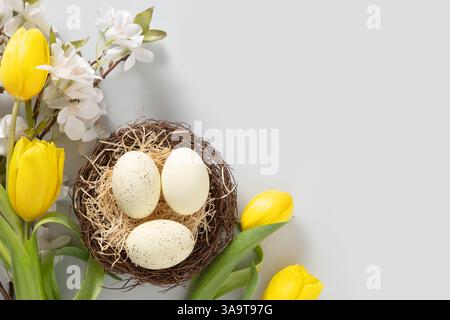 Easter eggs in nest and spring yellow tulips on gray background. View from above. Easter greeting card with copy space. Top view. Greeting card. Stock Photo