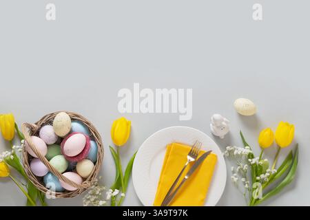 Easter frame with pastel colorful eggs, table setting decorated yellow tulip flowers on gray background. View from above. Flat lay. Happy Easter greet Stock Photo