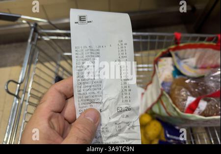 Frankfurt, Germany - Oct 24, 2023: Male hand holding a final receipt totaling 62,26 euros at German supermarket Edeka with a shopping cart and filled Stock Photo