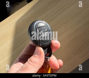 Paris, France - Mar 27, 2025: A hand holds a MINI key fob with integrated lock, unlock, and trunk buttons, featuring the MINI logo, set against a sunl Stock Photo