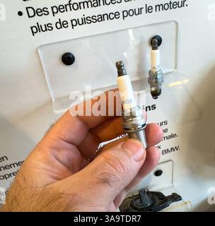 Paris, France - Mar 27, 2025: A hand holds a clean NGK spark plug in front of a white display at a dealership, with comparison units mounted on a tran Stock Photo