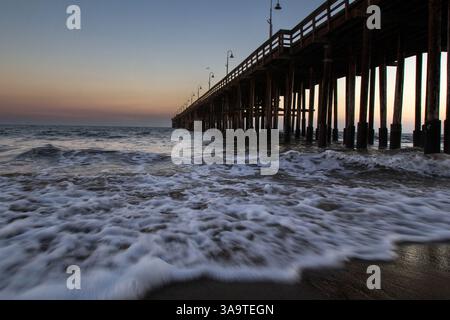 Ocean waves roll beneath Ventura Pier at twilight Stock Photo