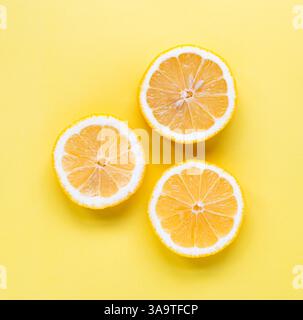 Overhead view of three slices of lemon on yellow background. Stock Photo