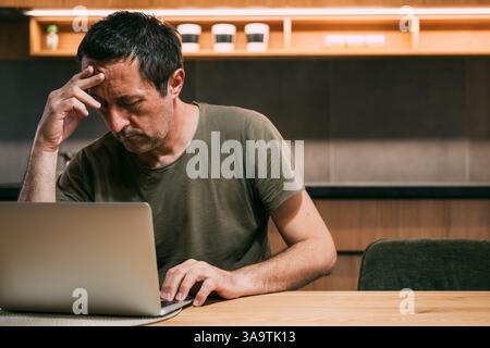 Tired exhausted freelancer working on a laptop computer late at night in home office, meeting the deadline for a remote job project, selective focus Stock Photo