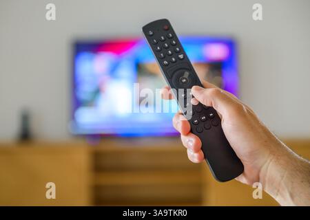 Male hand with a TV remote controller in living room, selective focus Stock Photo