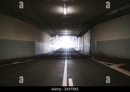 Bright light at the end of a dark,empty, underground tunnel road. Wide angle view, no people. Stock Photo