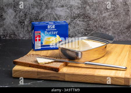 Neuwied, Germany - March 25,2025: a block of Weihenstephaner butter is placed on a wooden board, accompanied by a freshly sliced brown bread, a knife Stock Photo
