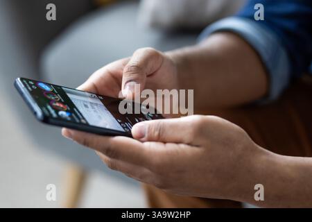 Close up of dark skinned hands holding and using a smartphone device to browse social media, connect, or play a game. Stock Photo