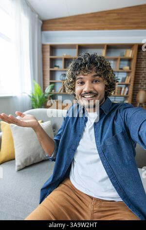 Phone webcam view. Man smiling and looking into camera, talking to colleagues and friends using smartphone app, sitting in living room on sofa. Stock Photo