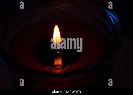 Beautiful burning candle with the flame reflection on the melted wax Closeup. Oil lantern. Blue splash on dark black background. Minimalistic concept. Stock Photo