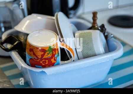 Clean dishes - cups, plates, bowls, cooking pot are getting dry in the broken blue washbowl at the camping kitchen. Drying utensils on the kitchen  co Stock Photo
