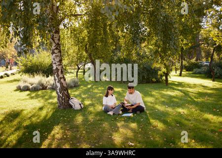 Couple enjoys reading together under a tree in a sunny park Stock Photo