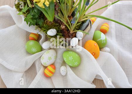 Colorful easter eggs on linen cloth and spring primroses in a pot. Easter still life Stock Photo