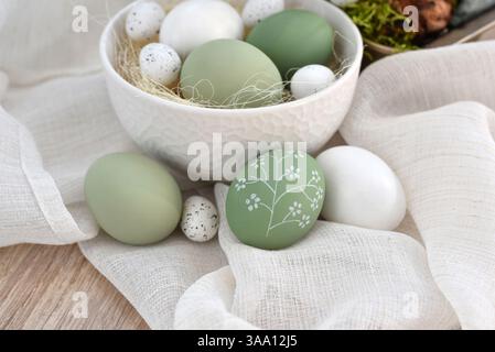 Stylish decorated easter eggs in a white bowl on linen cloth on a light wooden table. Happy Easter concept Stock Photo