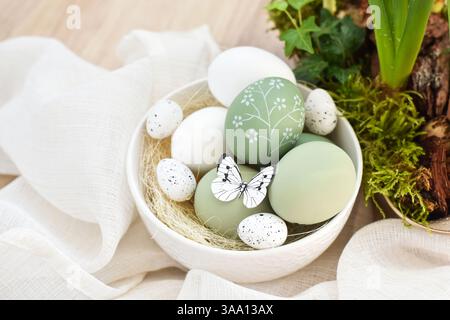 Stylish decorated easter eggs in a white bowl on linen cloth on a light wooden table. Happy Easter concept Stock Photo