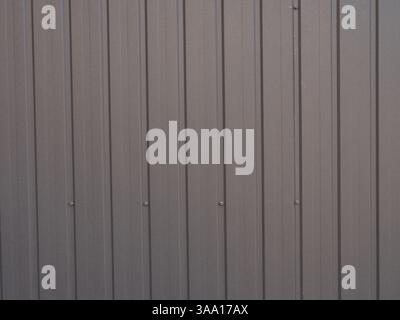 Gray metal fence or wall with vertical corrugated panels and visible bolts. Industrial-style surface with a uniform pattern. Backgrounds, construction Stock Photo