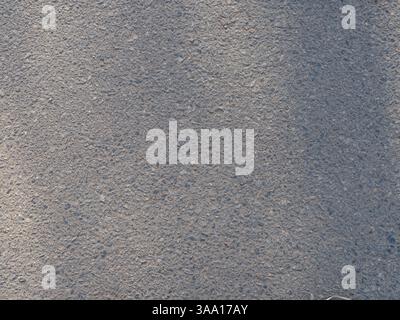 Close-up of asphalt surface with rough texture with small stones. Detailed structure of the pavement, with rugged and grainy appearance. Backgrounds, Stock Photo