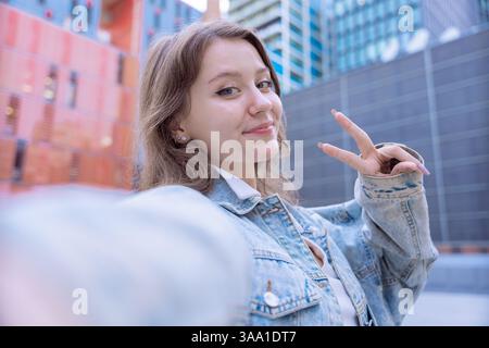 Caucasian student taking selfie and making peace sign in modern urban environment Stock Photo