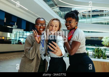 Excited young female recruits pose for a selfie in a stylish office, celebrating a new job opportunity with joy and teamwork. Stock Photo