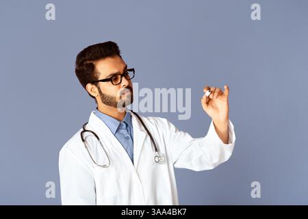 Serious Indian doctor writing with marker on virtual screen against lilac background, space for design Stock Photo