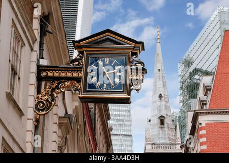 Vintage-style wall clock with Roman numerals hangs from an ornate bracket on a London street Stock Photo