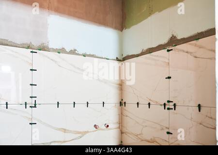 Beige marble tiles in the bathroom with plastic clips and wedges align large ceramic tiles on the wall. With space to copy. High quality photo Stock Photo