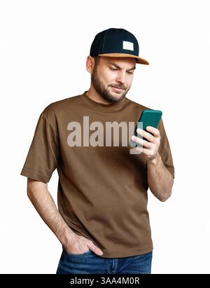 Isolated young man in brown t-shirt and snapback reading message on smartphone Stock Photo