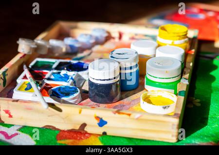 A beautifully crafted wooden box that is filled to the brim with various bottles of vibrant paint and an assortment of brushes Stock Photo