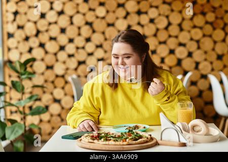 In a cozy cafe, a young woman with Down syndrome happily enjoys a tasty meal at her table. Stock Photo