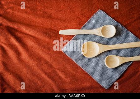 Set of wooden spoons arranged on a gray napkin over textured red fabric. Rustic and eco-friendly kitchen concept with warm tones, natural materials, a Stock Photo