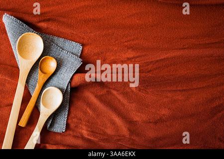 Set of wooden spoons arranged on a gray napkin over textured red fabric. Rustic and eco-friendly kitchen concept with warm tones, natural materials, a Stock Photo