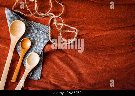 Wooden spoons on a gray napkin with natural jute twine, arranged on a textured red fabric background. Rustic and eco-friendly kitchen concept with war Stock Photo