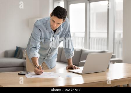 Man leaning over desk, making notes, focused on paperwork Stock Photo