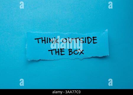 Think outside the box message written on ripped torn paper piece on blue background. Conceptual think outside the box symbol. Copy space. Stock Photo