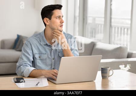 Man thinks, look aside while sit at desk with laptop Stock Photo