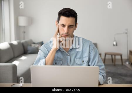 Young man deeply focused and thoughtful looks at laptop screen Stock Photo