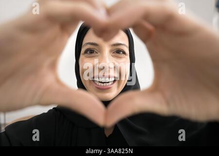 Arabic woman smiling through heart-shaped frame made with her hands Stock Photo