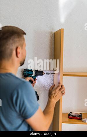 Young man assembling wooden shelf with electric drill while DIY and home renovation.Do It Yourself. High quality photo Stock Photo