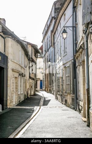 A narrow street with a blue sign on the left side in Cognac France. The street is lined with buildings and has a sidewalk Stock Photo