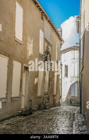 A narrow street with a blue sign on the left side in Cognac France. The street is lined with buildings and has a sidewalk Stock Photo