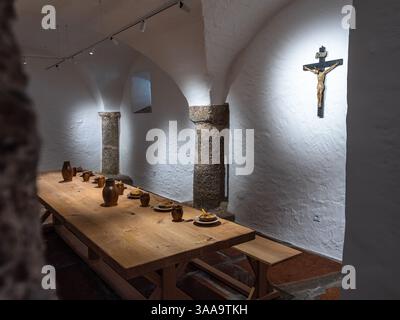 Michaelbeuern, Austria - October 22, 2024: Monastery rustic dining room with a long wooden table set with clay dishes and jugs. Crucifix on the whitew Stock Photo