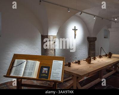 Michaelbeuern, Austria - October 22, 2024: A historical monastery dining room with a long wooden table set with pottery, open book on a stand, and a c Stock Photo