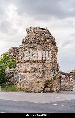 A large rock is sitting on the side of a road in Assisi city in Italy Umbria. The rock is covered in moss and has a few small plants growing on it Stock Photo
