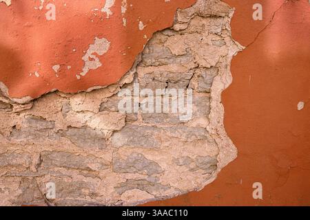 Cracked wall with rustic charm. A detailed close-up of a weathered wall with peeling red paint, revealing layers of plaster and brick underneath. Copy Stock Photo
